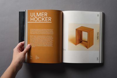 Aufgeschlagenes Buch. Linke Seite orange mit weißem Titel 'Ulmer Hocker' und Fließtext. Rechts Foto eines einfachen, geometrischen Hockers aus Holz.